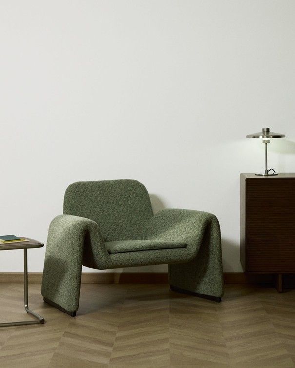 Groene stoffen fauteuil MELVIA in een kamer met houten vloer en bijzettafel.