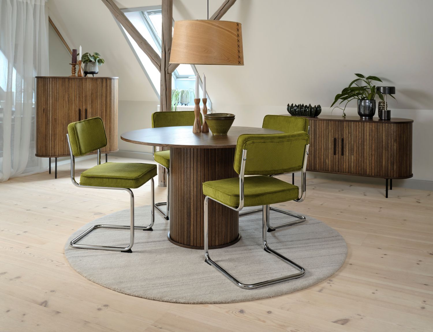 Vier eetkamerstoelen met stalen onderstel en groene suède zitting rond een ronde houten tafel.