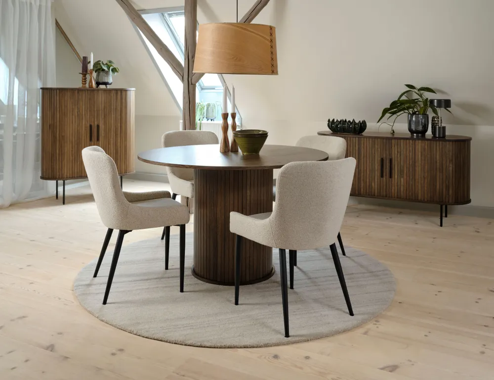 Ronde natural oak eetkamertafel NOLA met donkere houten poten, omringd door stoelen.