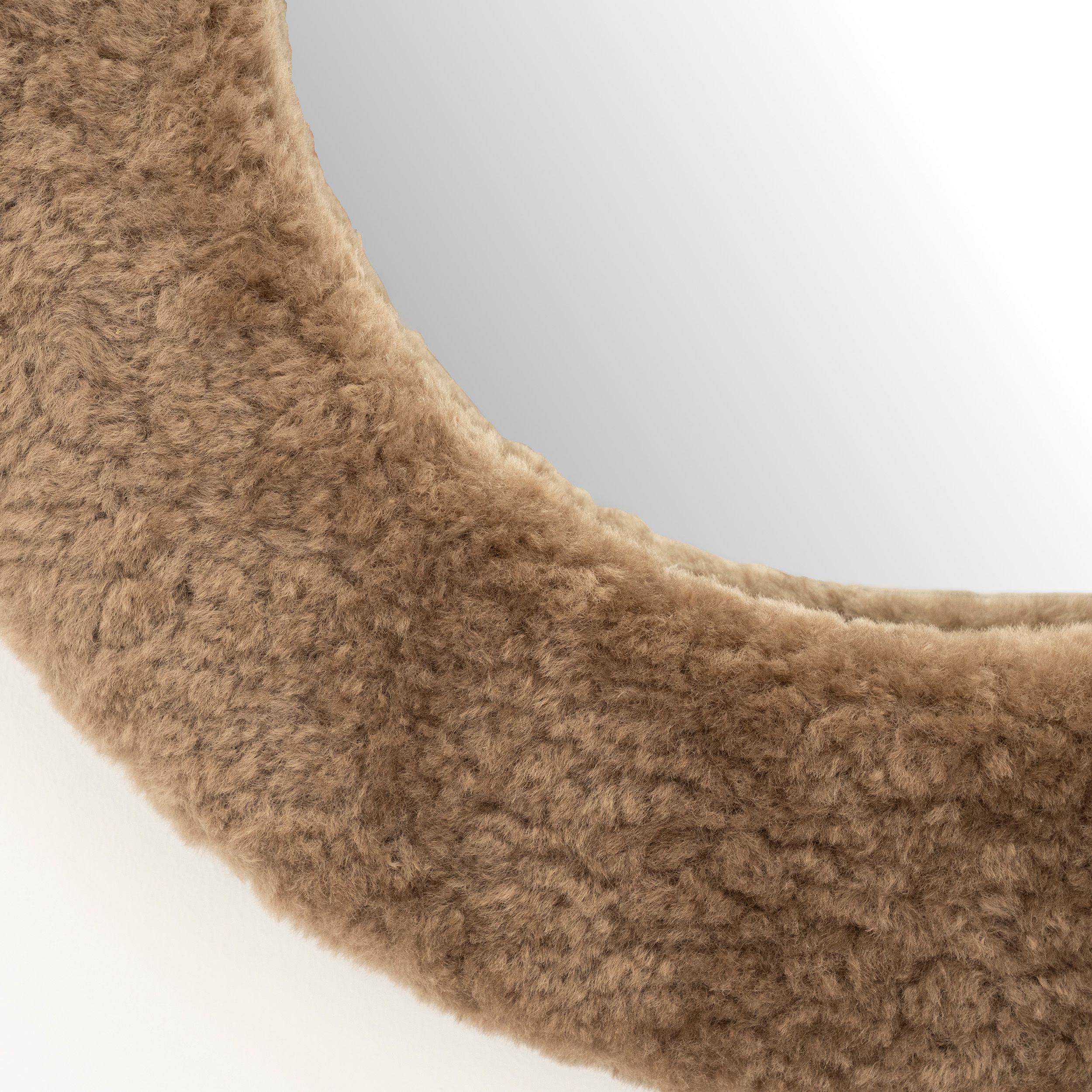 Ronde spiegel met beige, pluizige, stoffen rand, detailopname.
