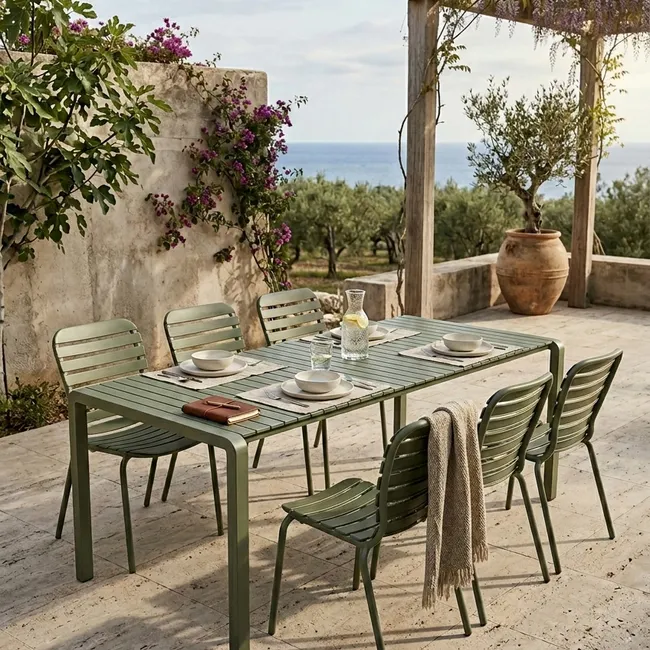 Groene metalen tuintafel met vier stoelen op een terras met uitzicht op zee.