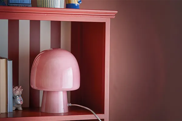 Roze paddestoelvormige tafellamp op een rood boekenrek met gestreepte achterwand.