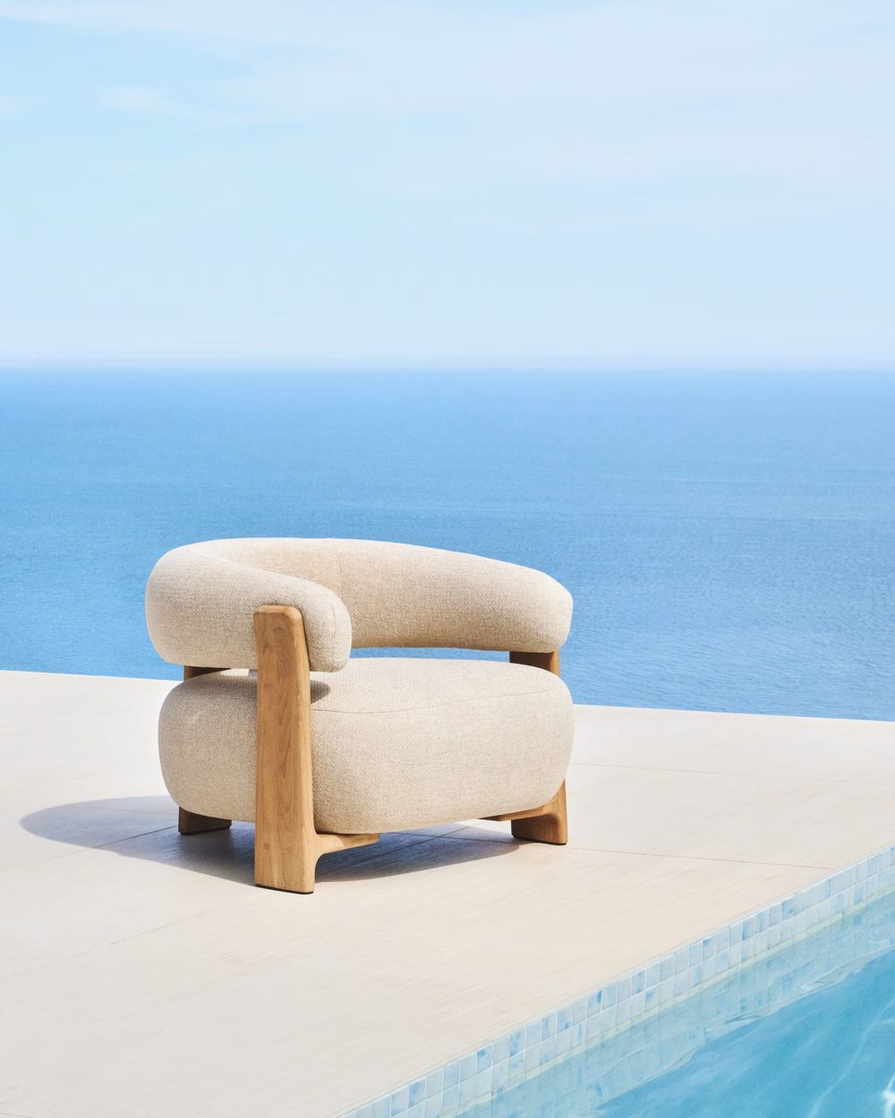 Loungefauteuil GRANITE - Beige met massief teakhouten frame bij een zwembad met uitzicht op zee.