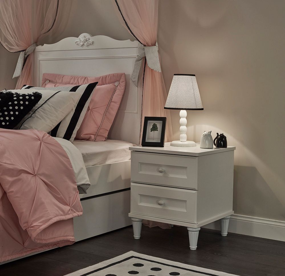 Wit houten nachtkastje LORA met twee lades naast een opgemaakt bed.