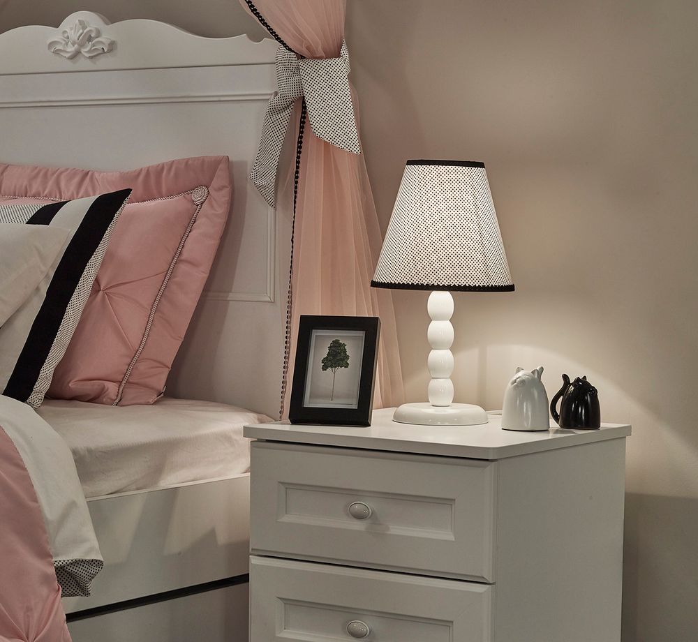 Wit houten nachtkastje LORA met twee lades naast een wit bed in een kinderkamer.