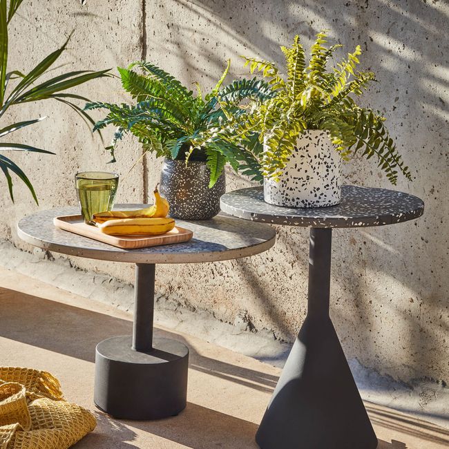 Bijzettafel DELANO zwart, blad van terrazzo, met glas en bananen op een houten plank.