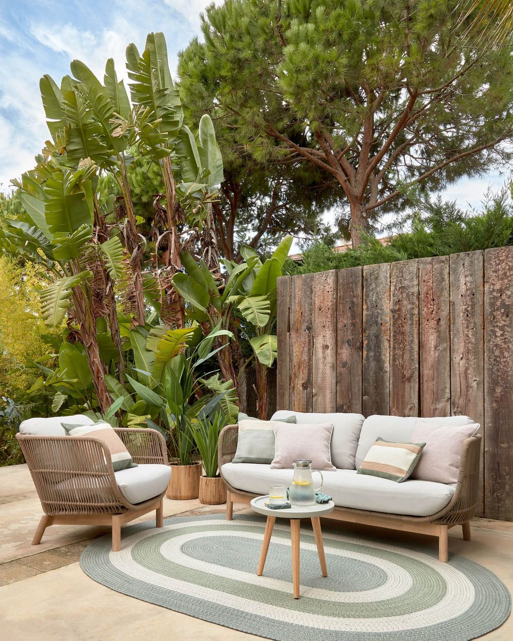 Loungefauteuil en bank CATALINA in beige/acaciahout op een terras met planten.