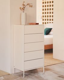 Witte houten commode met vijf lades en metalen poten, met vaas en doosje erop, in een slaapkamer.