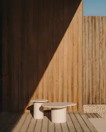 Twee roomwitte bijzettafels, de ene rond en de andere organisch, voor een houten wand.