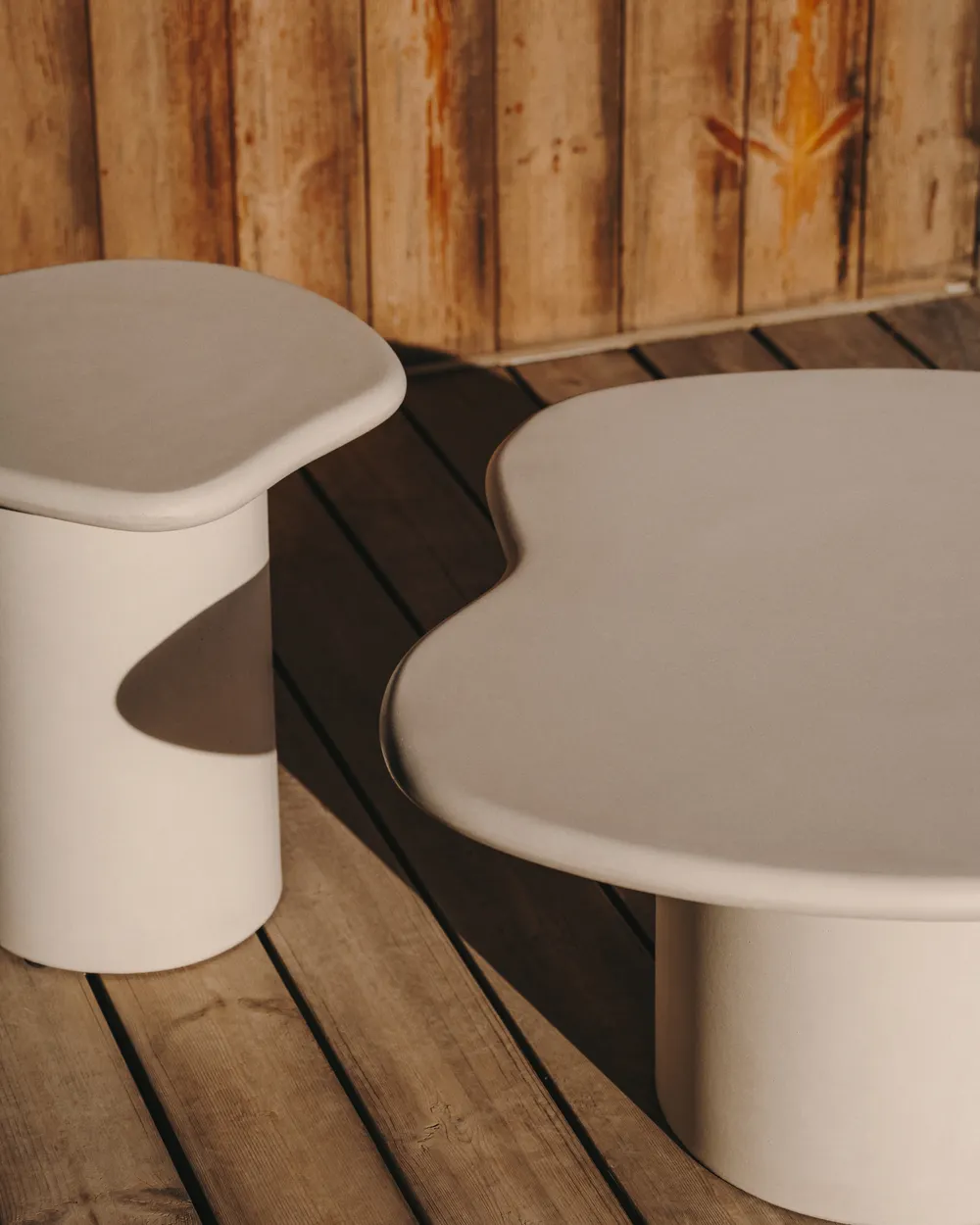 Twee organisch gevormde cementen tafels, één bijzettafel en één salontafel, met een lichte mokka kleur.