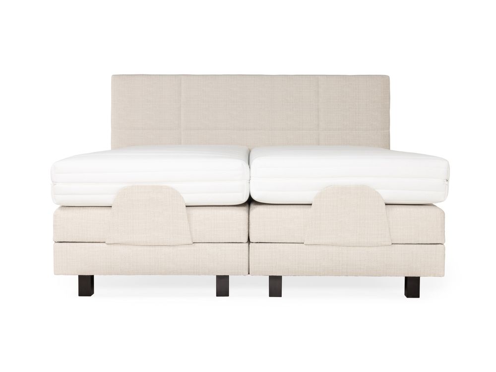 Crèmekleurige elektrische boxspring met beige stoffen bekleding en twee witte matrassen.