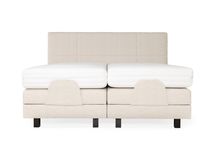 Crèmekleurige elektrische boxspring met beige stoffen bekleding en twee witte matrassen.