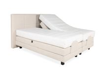 Elektrische boxspring firm met beige textiel bekleding, één matras is versteld.
