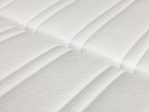 Detail van een wit gestoffeerd matras met stiknaden.