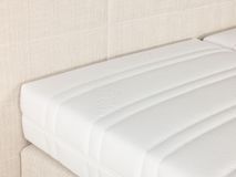 Crèmekleurige boxspring met beige stoffen hoofdbord en wit matras met geribde structuur.