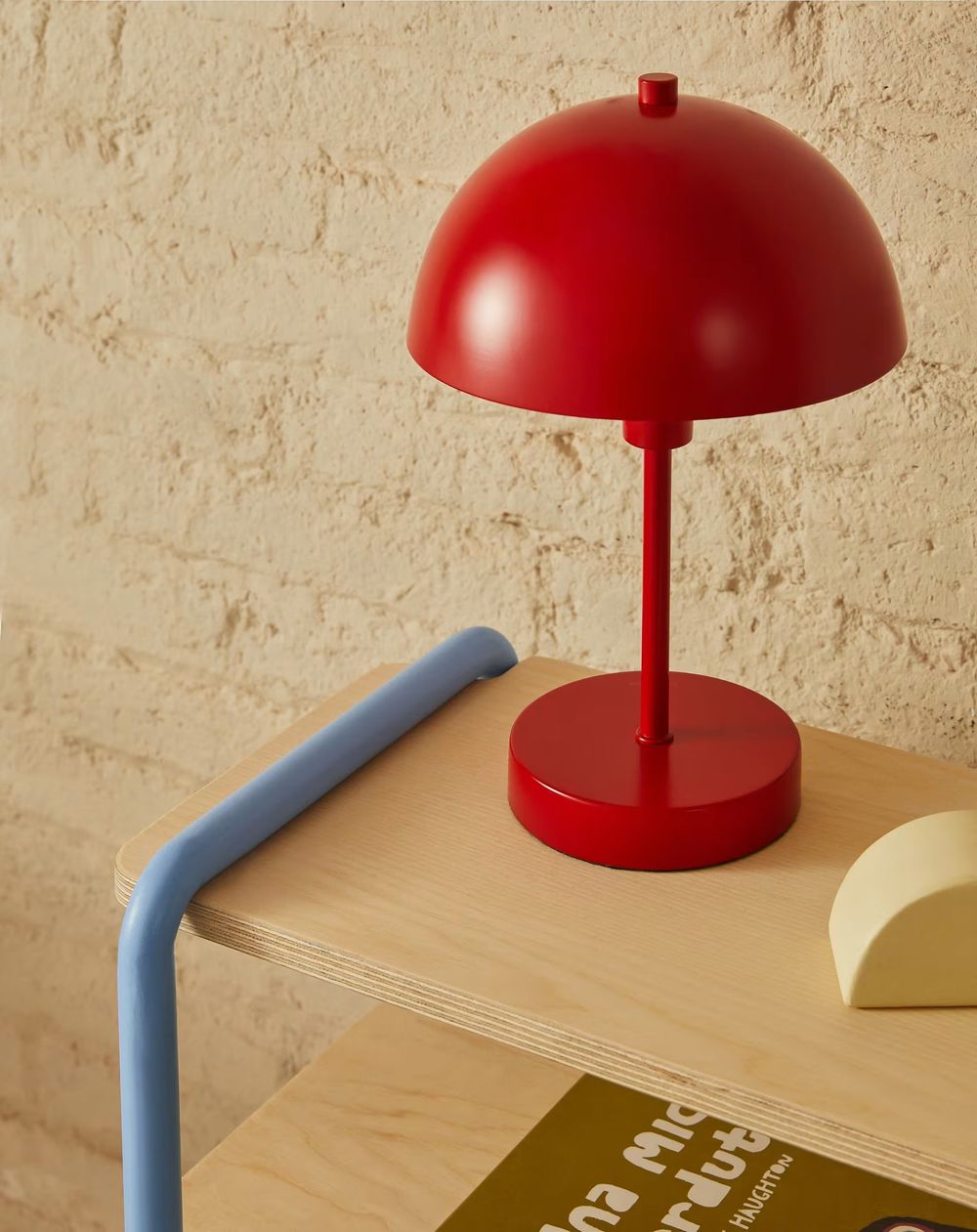 Rode metalen tafellamp ORONJA met bolle kap en ronde voet op houten plank.