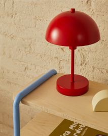 Rode metalen tafellamp ORONJA met bolle kap en ronde voet op houten plank.