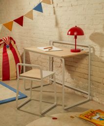Rode, metalen tafellamp met halfronde kap op een lichte houten bureau met wit metalen frame.