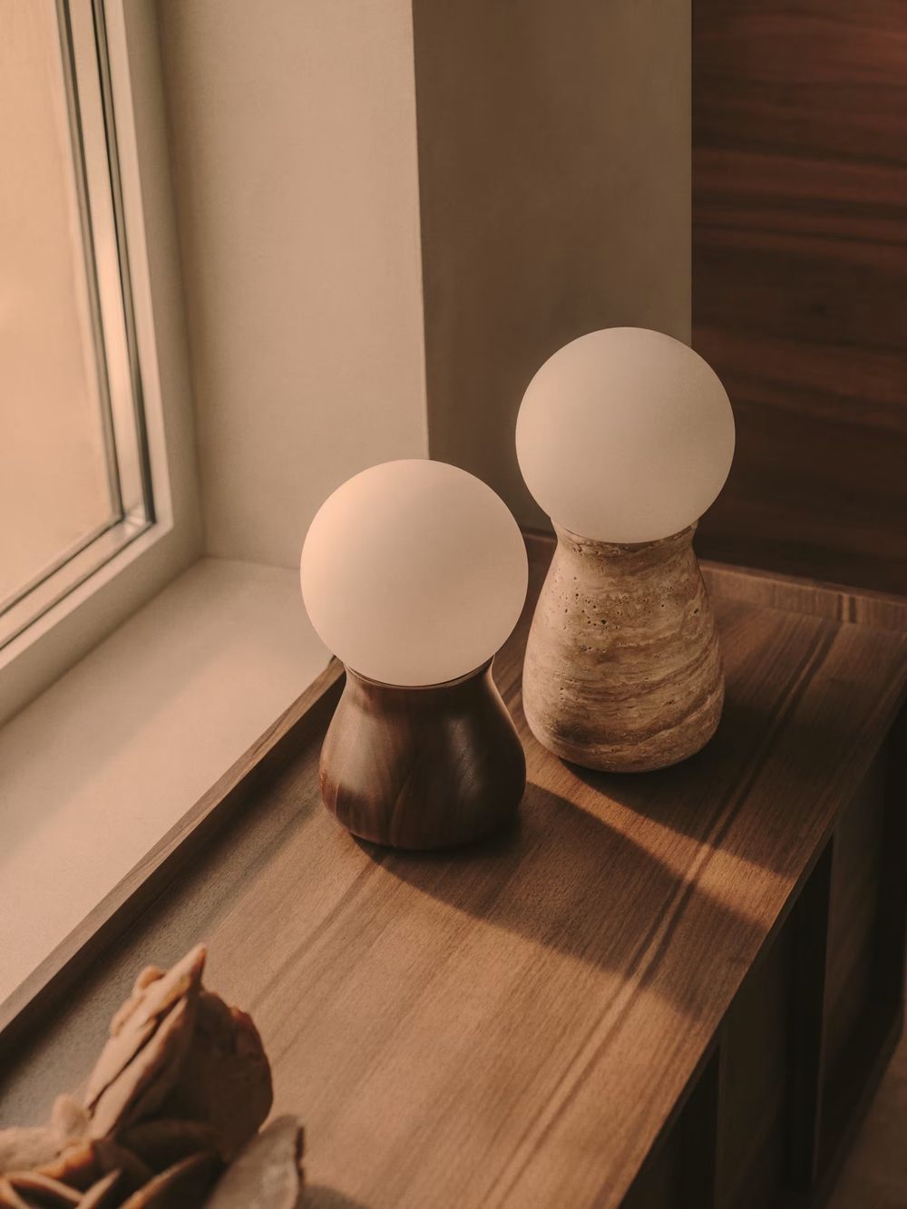 Tafellamp OKENI met een houten voet en een met travertijn afgewerkte voet, beide met een witte glazen bol.
