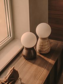 Tafellamp OKENI met een houten voet en een met travertijn afgewerkte voet, beide met een witte glazen bol.