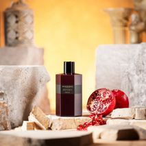 Bordeauxrode glazen flacon parfum ‘MANDARINE SULTANE’ met verse, opengesneden granaatappel.