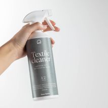 Hand houdt witte spuitfles met donkergrijze, witte en zwarte tekst van 500 ml textielreiniger vast.