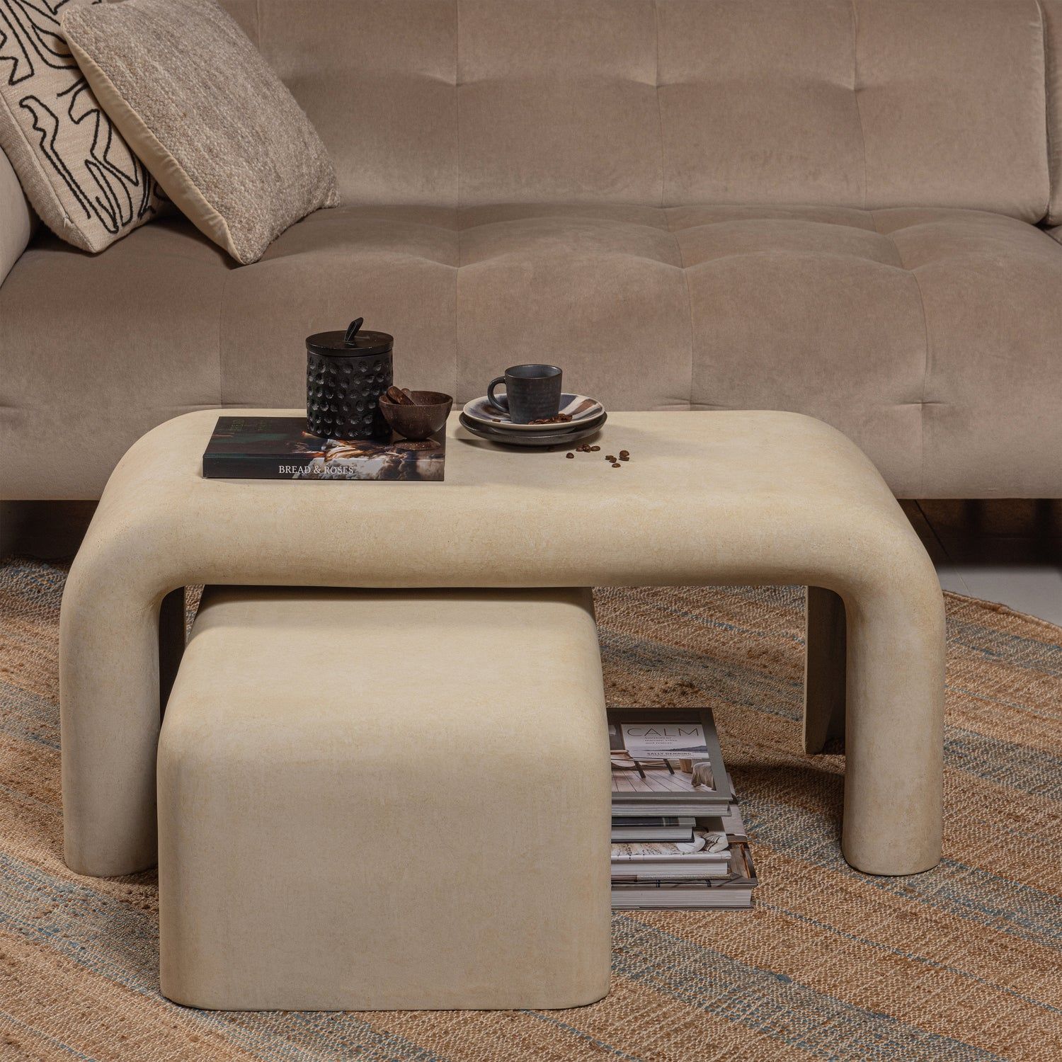 Set van 2 beige salontafels van betonlook materiaal, met een kleiner exemplaar eronder geschoven.