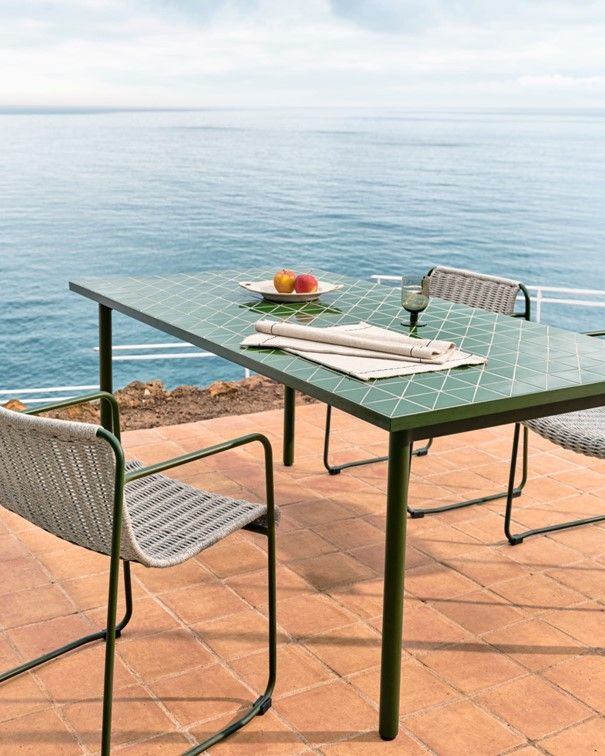 Groene metalen tuintafel met twee stoelen op een terras aan zee.