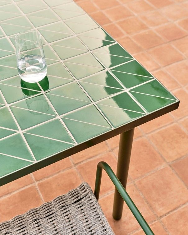 Groene tuintafel Maurina met tegelblad en een glas water, op een terras.